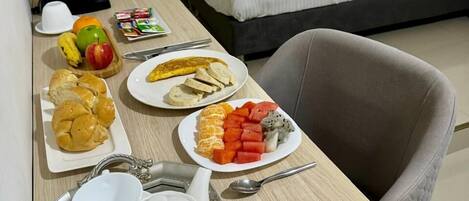Habitación de hotel con cama, escritorio con productos de desayuno, cafetera y una silla.