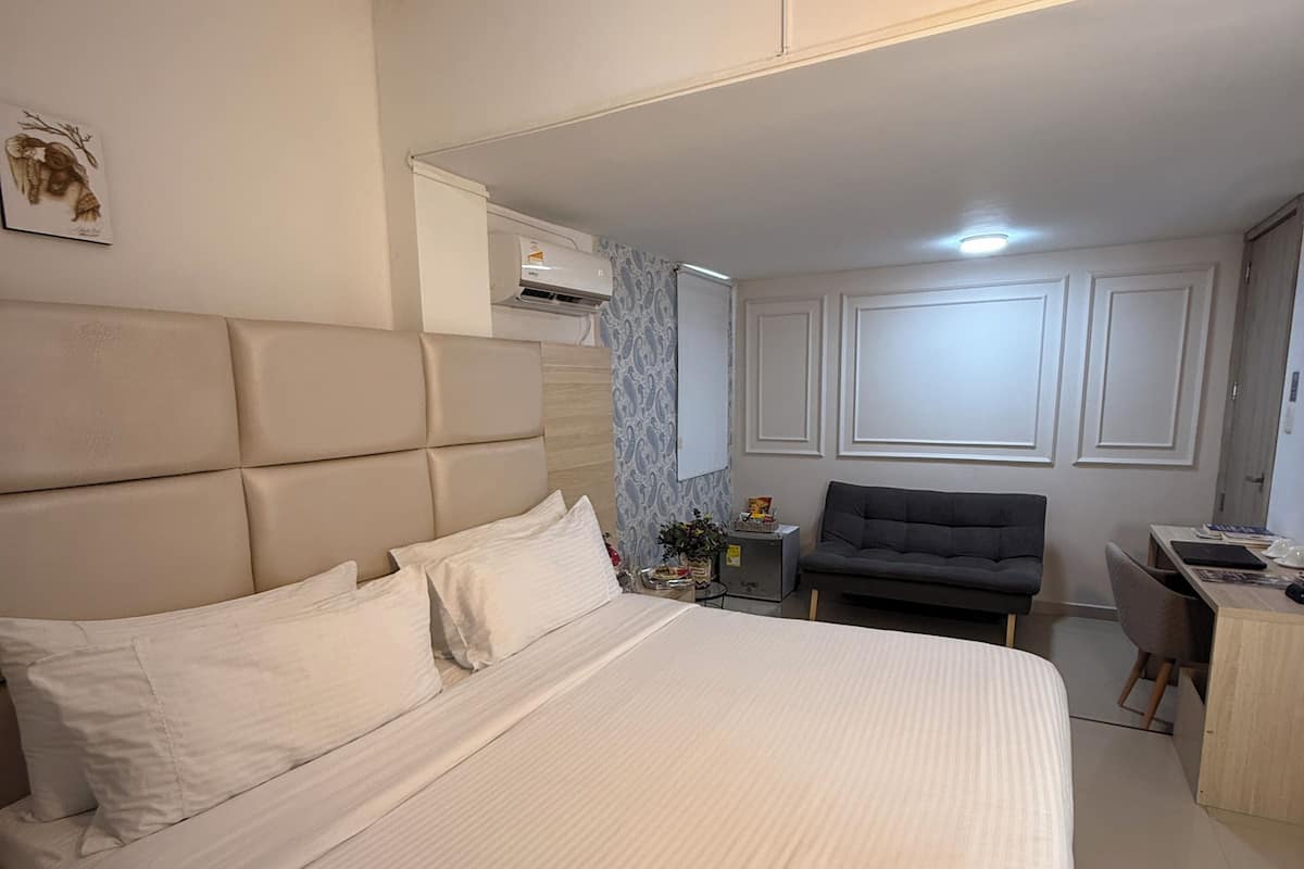 Une chambre dotée d’un grand lit, d’un bureau, d’une chaise, d’un climatiseur et d’un ventilateur de plafond.