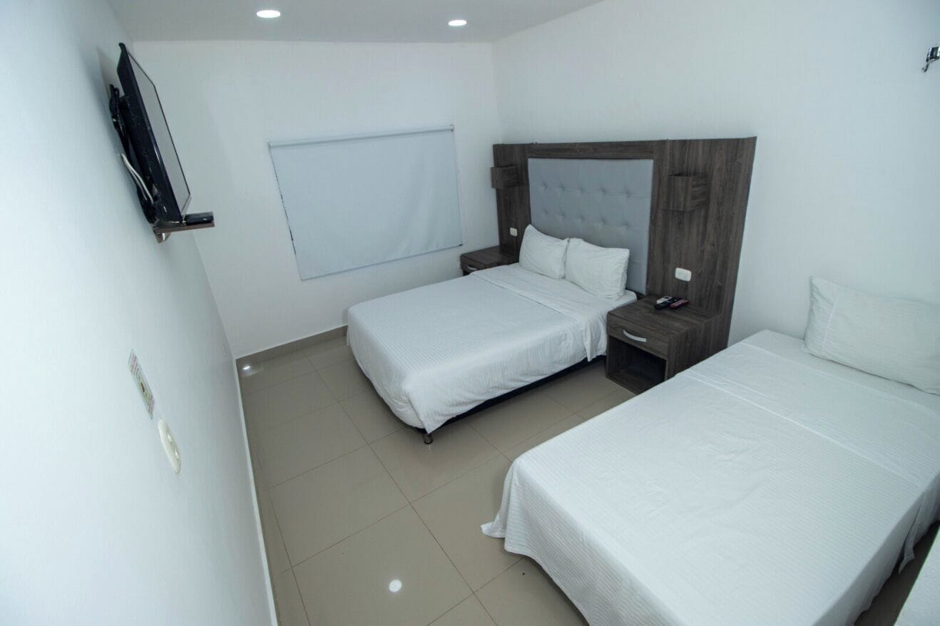Een hotelkamer met twee bedden, een aan de muur bevestigde televisie en een raam met een zonnescherm.