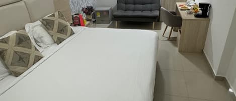 Habitación de hotel con una cama grande, un sofá, un escritorio con silla y un televisor en la pared.