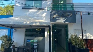 A modern hotel with a two-story structure, a covered outdoor seating area with tables and chairs, and potted plants. - HOTEL JUAN PABLO II (Riohacha)