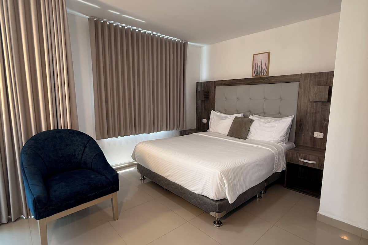 Une chambre d’hôtel moderne, équipée d’un lit, d’une chaise, d’une table de chevet et d’un luminaire au plafond.
