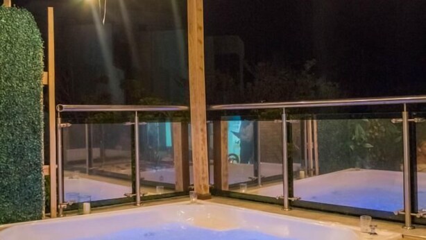 A hot tub area with wooden beams and glass railings, surrounded by a wooden deck with rose petals. - HOTEL JUAN PABLO II (Riohacha)