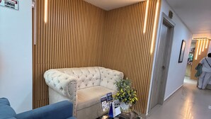 A modern interior with a tufted sofa, a blue armchair, a glass coffee table with brochures, and a wooden slat wall. - HOTEL JUAN PABLO II (Riohacha)