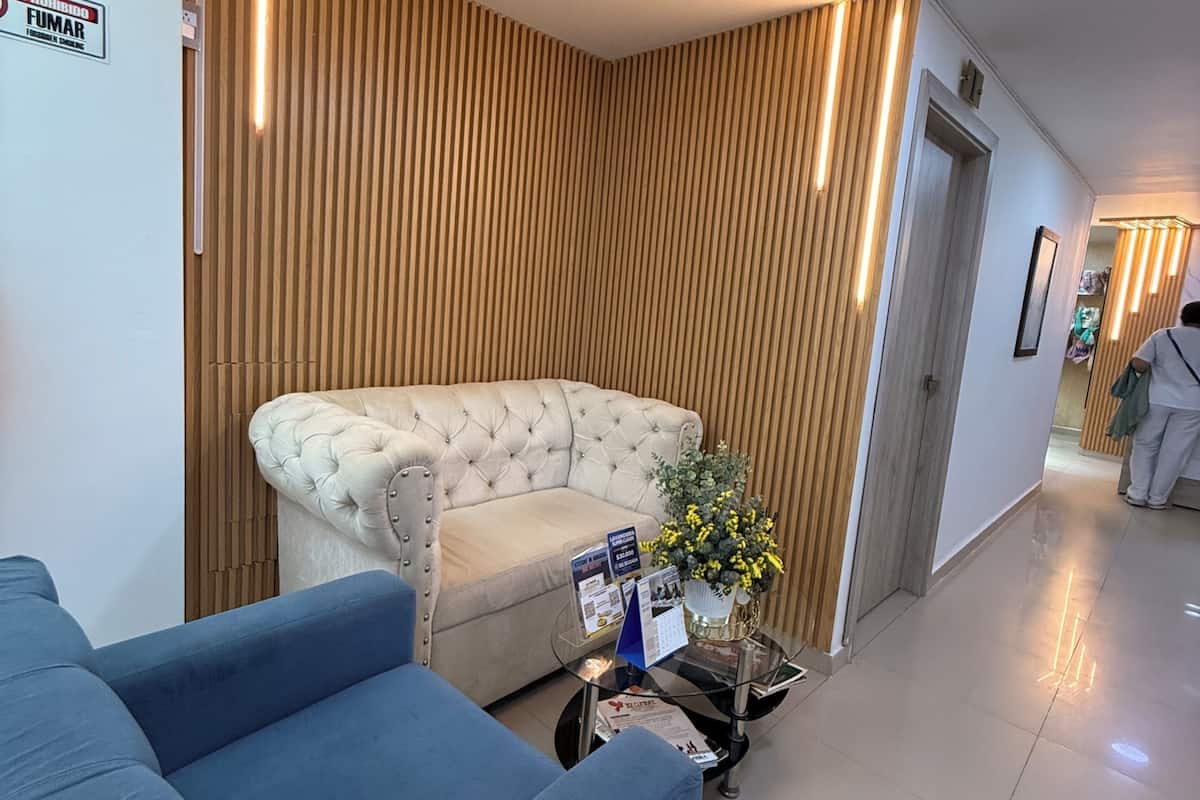 Un intérieur moderne avec un canapé capitonné, un fauteuil bleu, une table basse en verre sur laquelle sont posées des brochures, et un mur fait de lattes de bois.