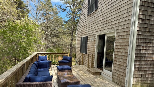A wooden deck with wicker furniture and a glass door leading to a covered area.