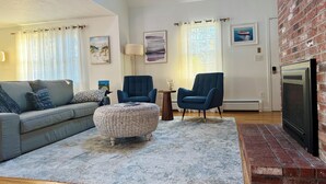 A living room with a grey sofa, blue armchairs, a woven ottoman, and a fireplace.