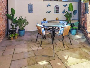 A patio with a round table and chairs, surrounded by potted plants and decorative wall art. - 1 bedroom accommodation in Filey (Filey)