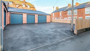 A parking area with two blue garage doors, a brick building with a sloped roof, and a wooden fence.