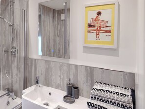 A modern bathroom with a large mirror, a white sink, a shower, and a framed picture on the wall. - 1 bedroom accommodation in Filey (Filey)
