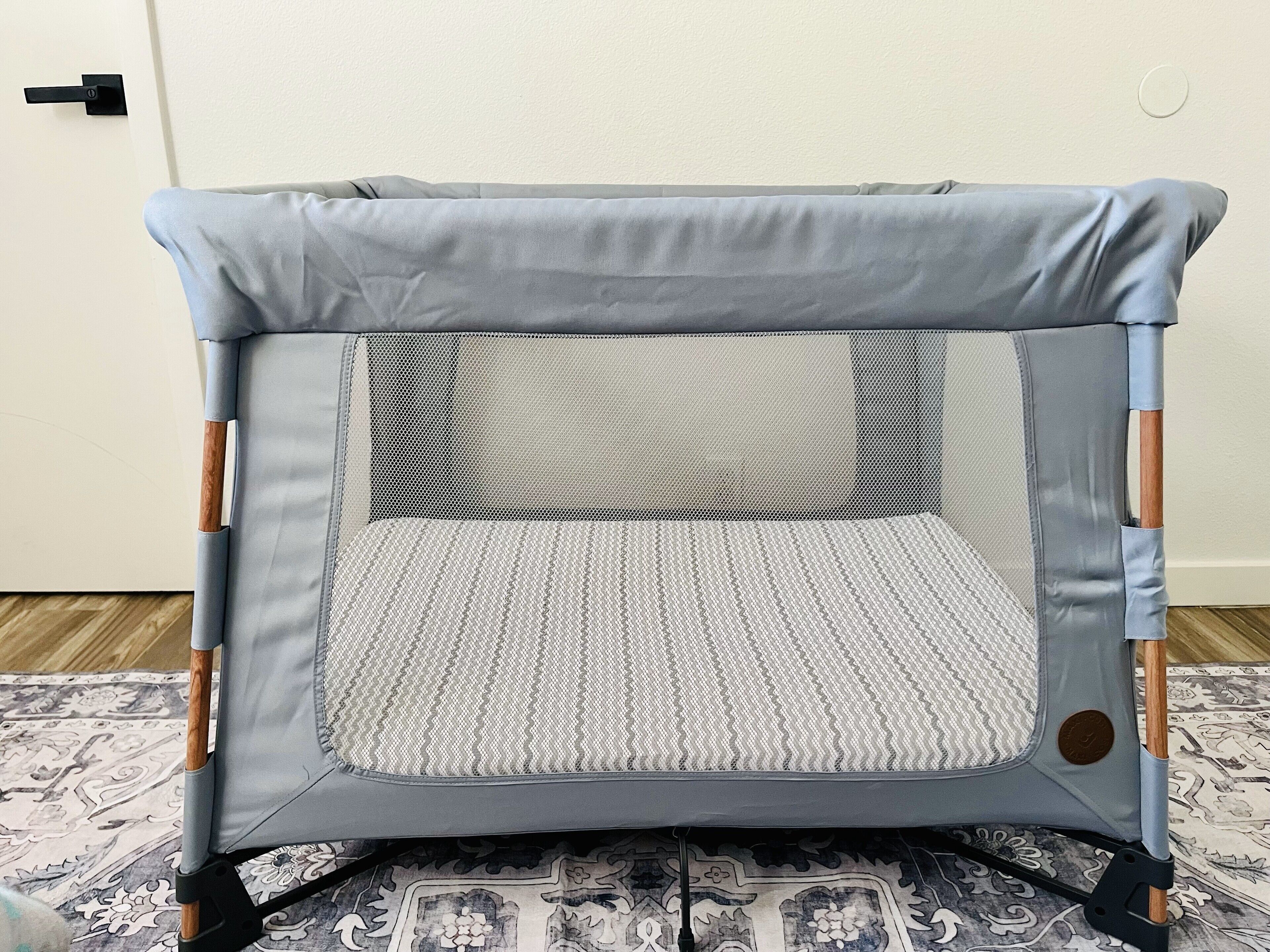 A baby playpen with a mesh back and padded floor, featuring wooden accents on the sides.