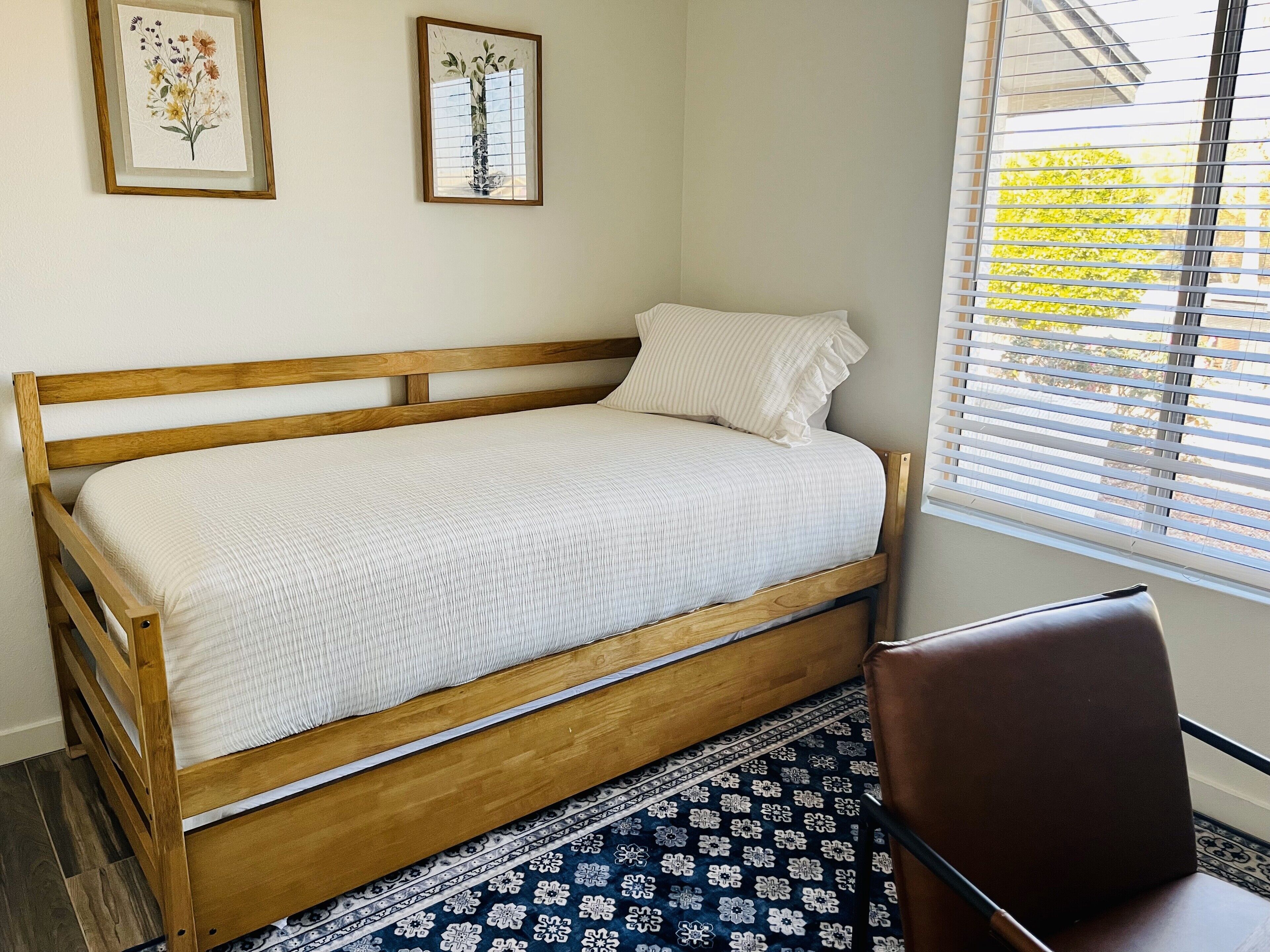 Un lit simple avec un cadre en bois, une couvre-lit blanche et un tapis à motifs sur le sol.