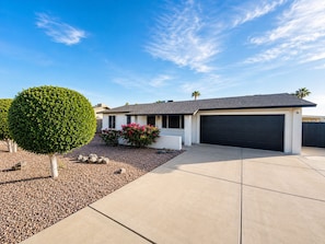A modern two-story house with a garage, a well-maintained lawn, and a large tree.