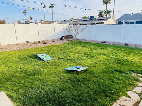 A grassy backyard with two blue lawn games, a white fence, and solar panels on rooftops.