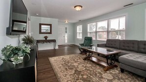 A living room with a sofa, a coffee table, a chair, a TV, and a large window. - Charming 4-bedroom house with AC and WiFi in delightful Troutman (Troutman)