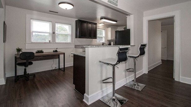 A modern kitchen with dark wood cabinets, a central island with bar stools, a built-in oven, and a large window providing natural light. - Charming 4-bedroom house with AC and WiFi in delightful Troutman (Troutman)