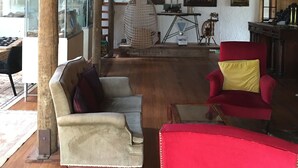 A spacious room with wooden beams on the ceiling, a red armchair, a beige sofa, and a hanging chair. - Rustic barn on organic farm in South Head (South Head)