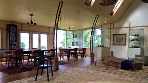 A spacious living room with a large wooden dining table, multiple chairs, a fireplace, and a bookshelf. - Rustic barn on organic farm in South Head (South Head)