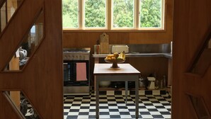 A kitchen with a checkered floor, a table with fruits, and a window with a view of greenery. - Rustic barn on organic farm in South Head (South Head)