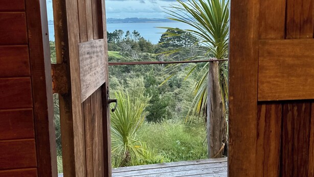A wooden door opening to a balcony with a view of a body of water and greenery. - Rustic barn on organic farm in South Head (South Head)