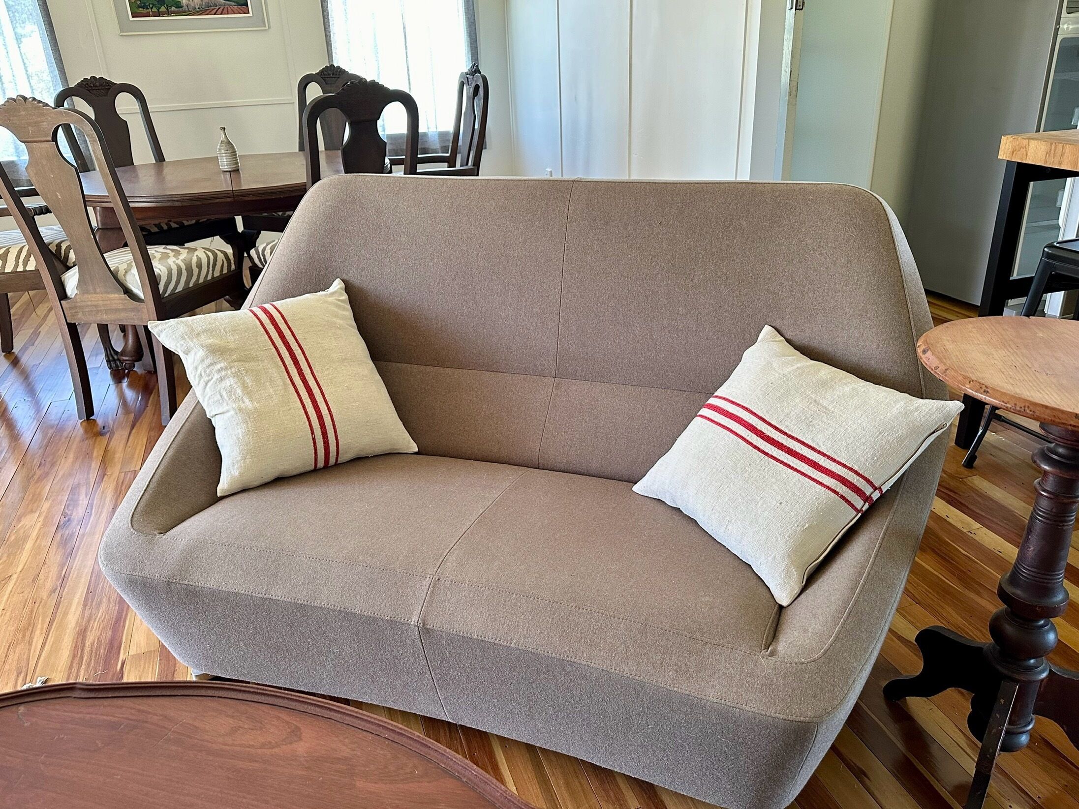 A beige sofa with two pillows, a wooden dining table, and chairs in a room with wooden flooring.