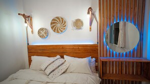A bedroom with a wooden headboard, a bed with white linens, and three wall-mounted woven wall hangings. - Paddle Out Morocco (Tamraght)