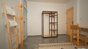 A room with a wooden chair, a standing wooden chair with a towel, a metal shelf unit, and a wooden door. - Paddle Out Morocco (Tamraght)