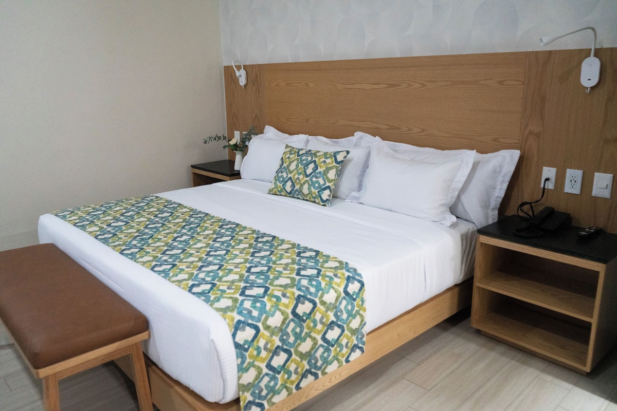 A neatly made bed with a patterned bedspread, a wooden headboard, and a bedside table with a lamp.