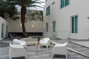 A modern outdoor seating area with white chairs, a palm tree, and a pool.