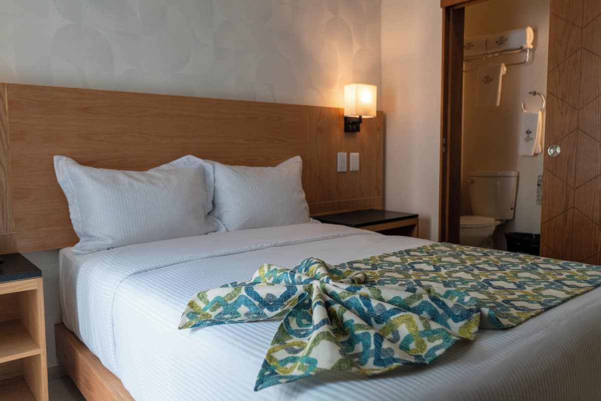 A neatly made bed with a patterned throw, a wooden headboard, and a wall-mounted light fixture.