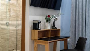 Un baño moderno con cabina de ducha de vidrio, tocador de madera con encimera negra, cafetera, un florero con una rosa roja y una silla negra.