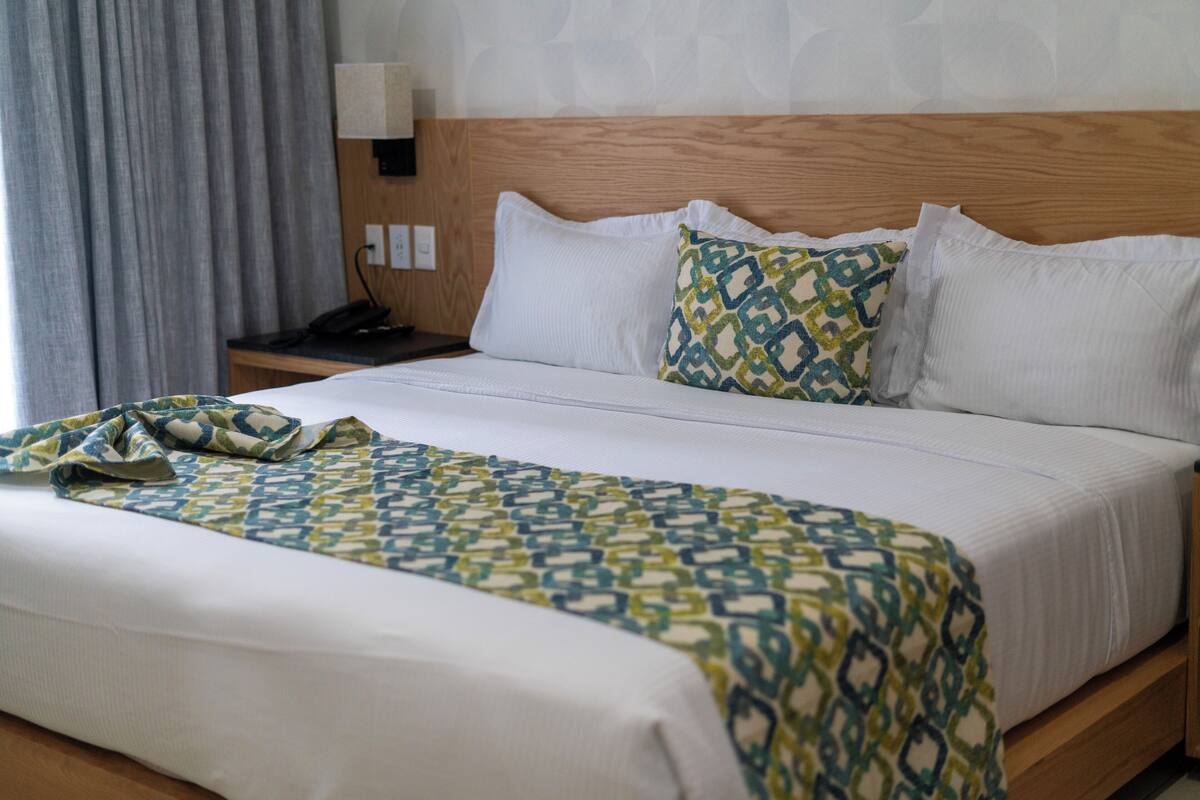 A hotel room with a wooden headboard, a white bedspread, and a patterned throw blanket.