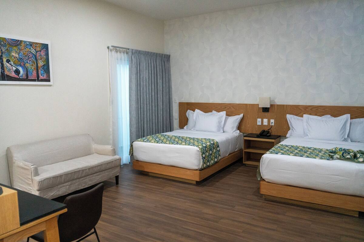 A hotel room with two beds, a sofa, a desk, and a chair.