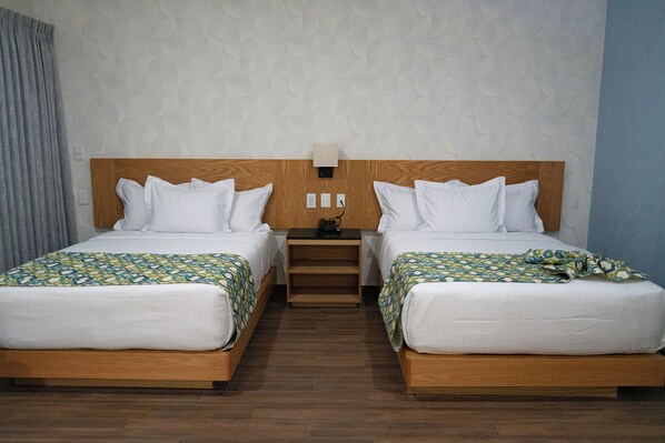 A hotel room with two beds, wooden headboards, a nightstand, and a wall-mounted lamp.