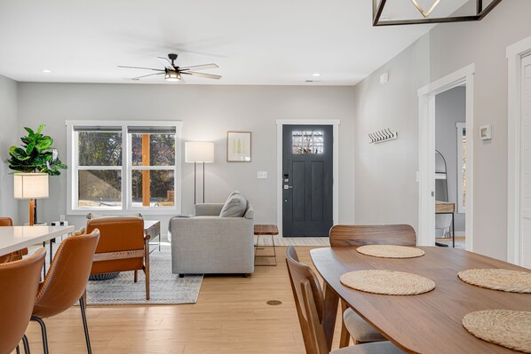 Una sala de estar moderna con un sofá gris, una mesa de comedor con individuales y un ventilador de techo.