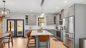 A modern kitchen with grey cabinets, stainless steel appliances, and a central island with bar stools. - NEW Dream Weaver - 5 min Walk to Main Street! (Weaverville)