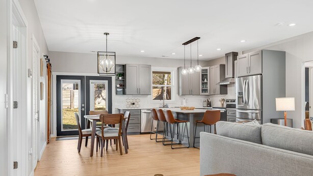 A modern kitchen with grey cabinets, stainless steel appliances, and a dining area with wooden chairs and a bench. - NEW Dream Weaver - 5 min Walk to Main Street! (Weaverville)