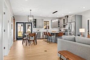 Una cocina moderna con armarios grises, electrodomésticos de acero inoxidable y una zona de comedor con sillas y un banco de madera.