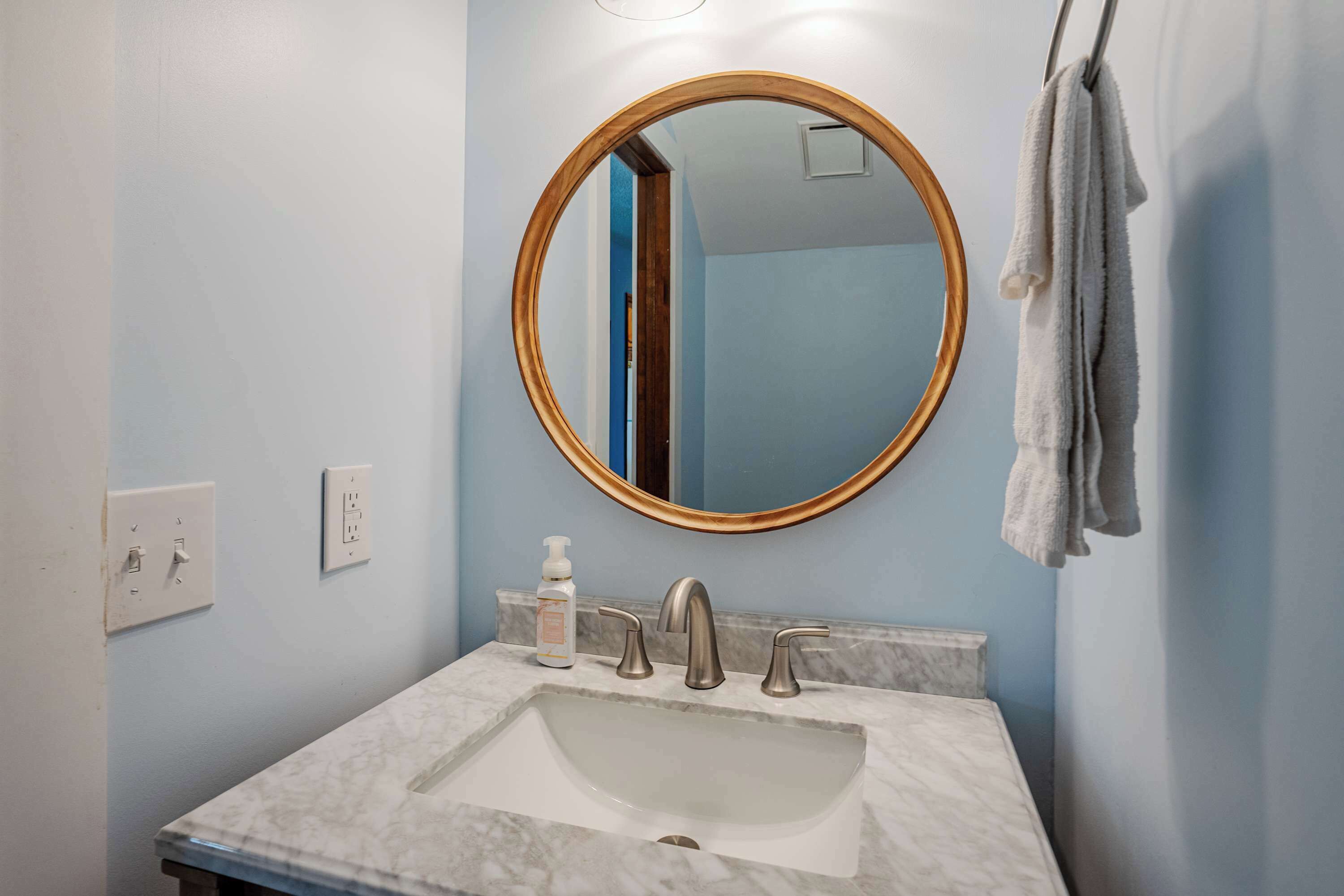 A bathroom with a marble sink, a round mirror, and a towel hanging on a rack.