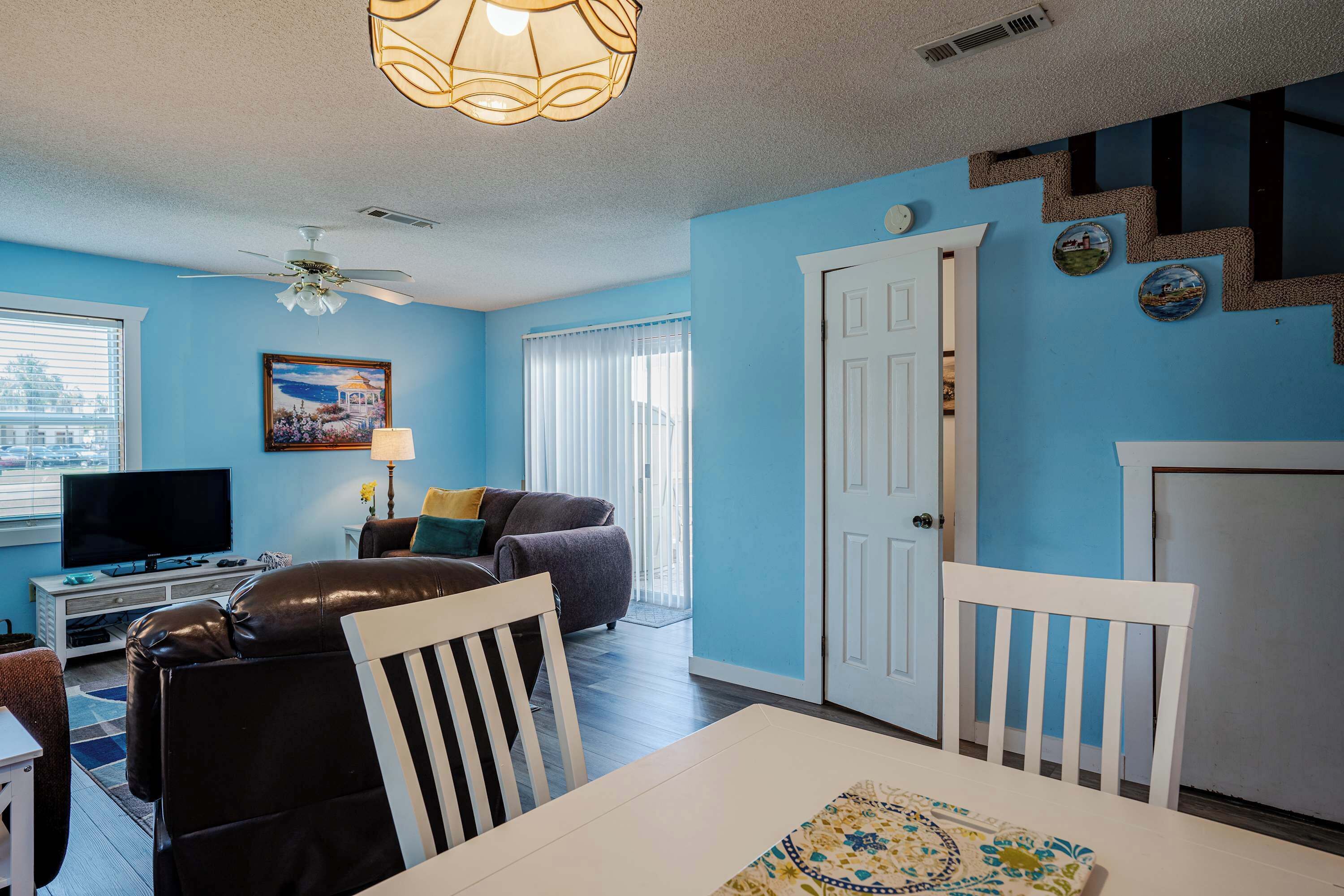 A living room with a television, a ceiling fan, a dining table, and a white door.