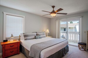 A bedroom with a bed, nightstand, lamp, ceiling fan, and a view through a sliding glass door.