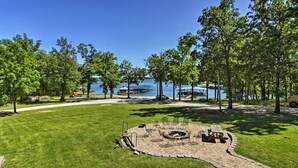 A circular outdoor seating area with a fire pit, surrounded by a paved walkway, overlooking a lake with docks and boats. - Poolside | Lake Views | Game Room | 2-Min to SDC (Branson)