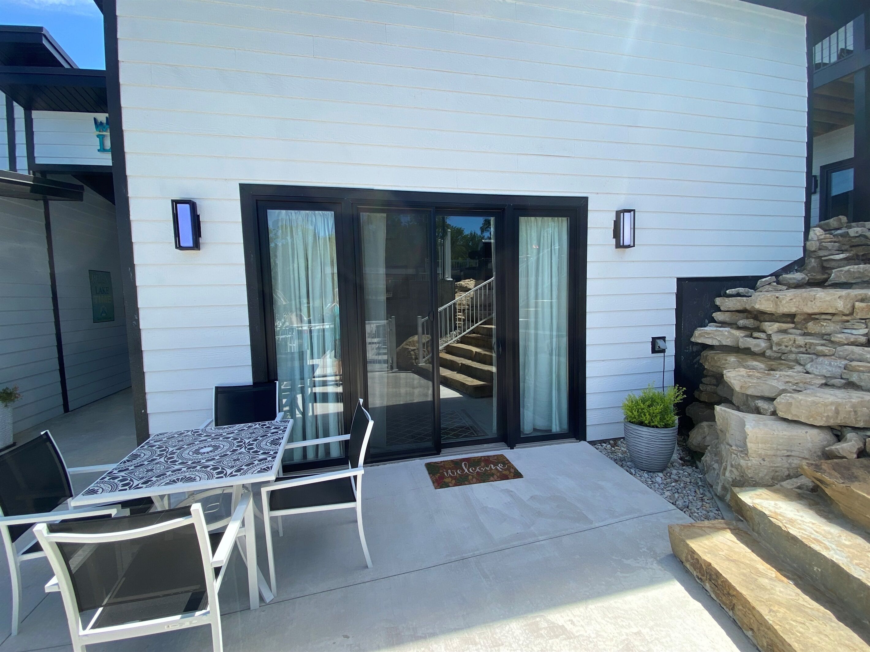 A patio with a table and chairs, a stone wall, and a staircase leading to a second floor.