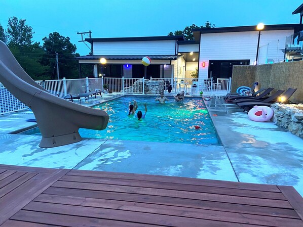 Una piscina con tobogán, sillas de descanso y una terraza.