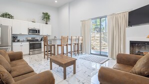 A modern living room with a fireplace, a dining area with wooden chairs, and a kitchen with white cabinets and stainless steel appliances. - Poolside | Lake Views | Game Room | 2-Min to SDC (Branson)