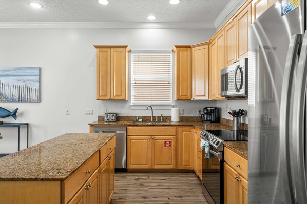 A modern kitchen with wooden cabinets, granite countertops, stainless steel appliances, and a window with blinds. - Palm Breeze Retreat Sleeps 10! (Panama City Beach)