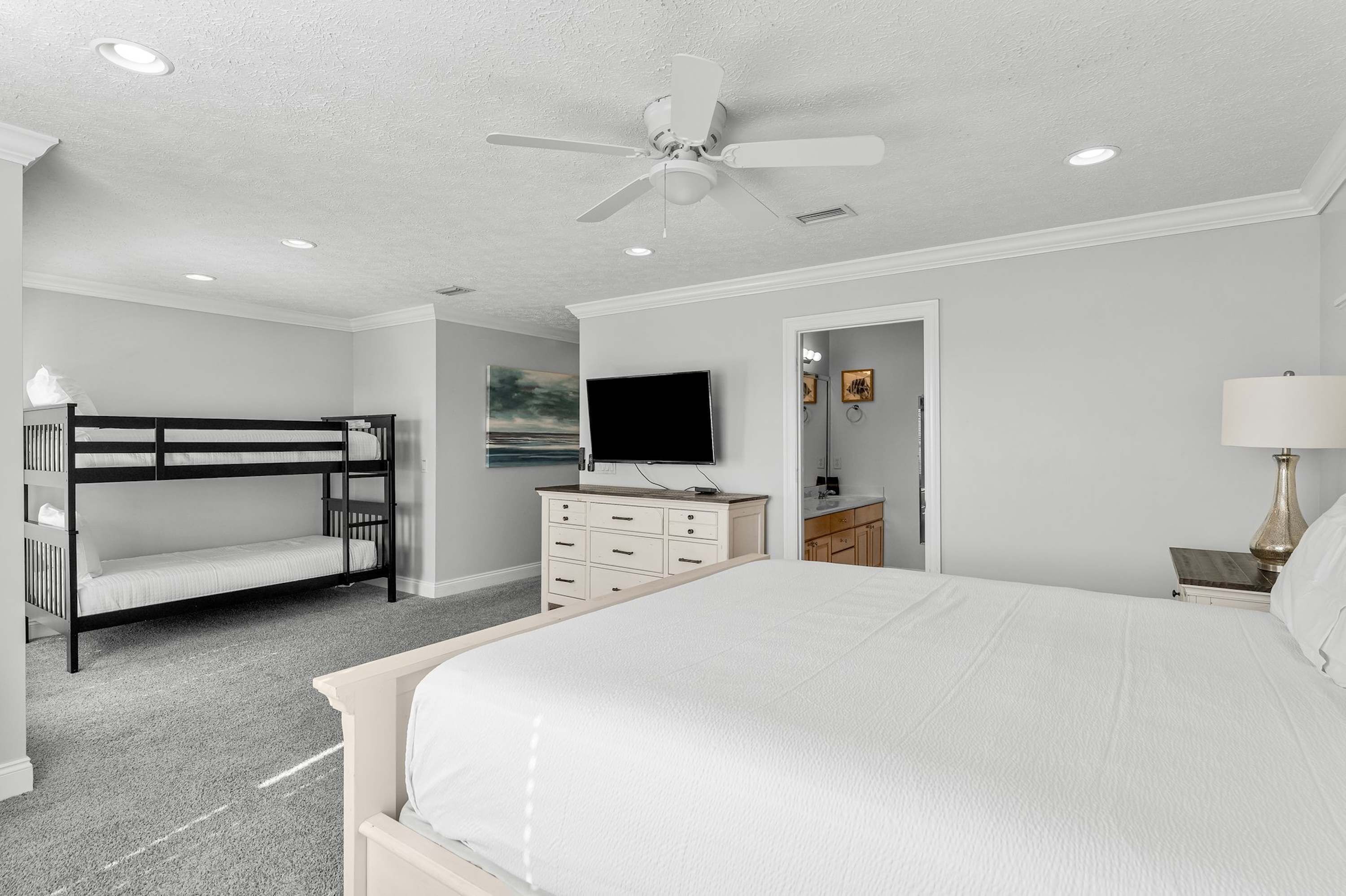 A bedroom with bunk beds, a dresser, a TV, and a ceiling fan.