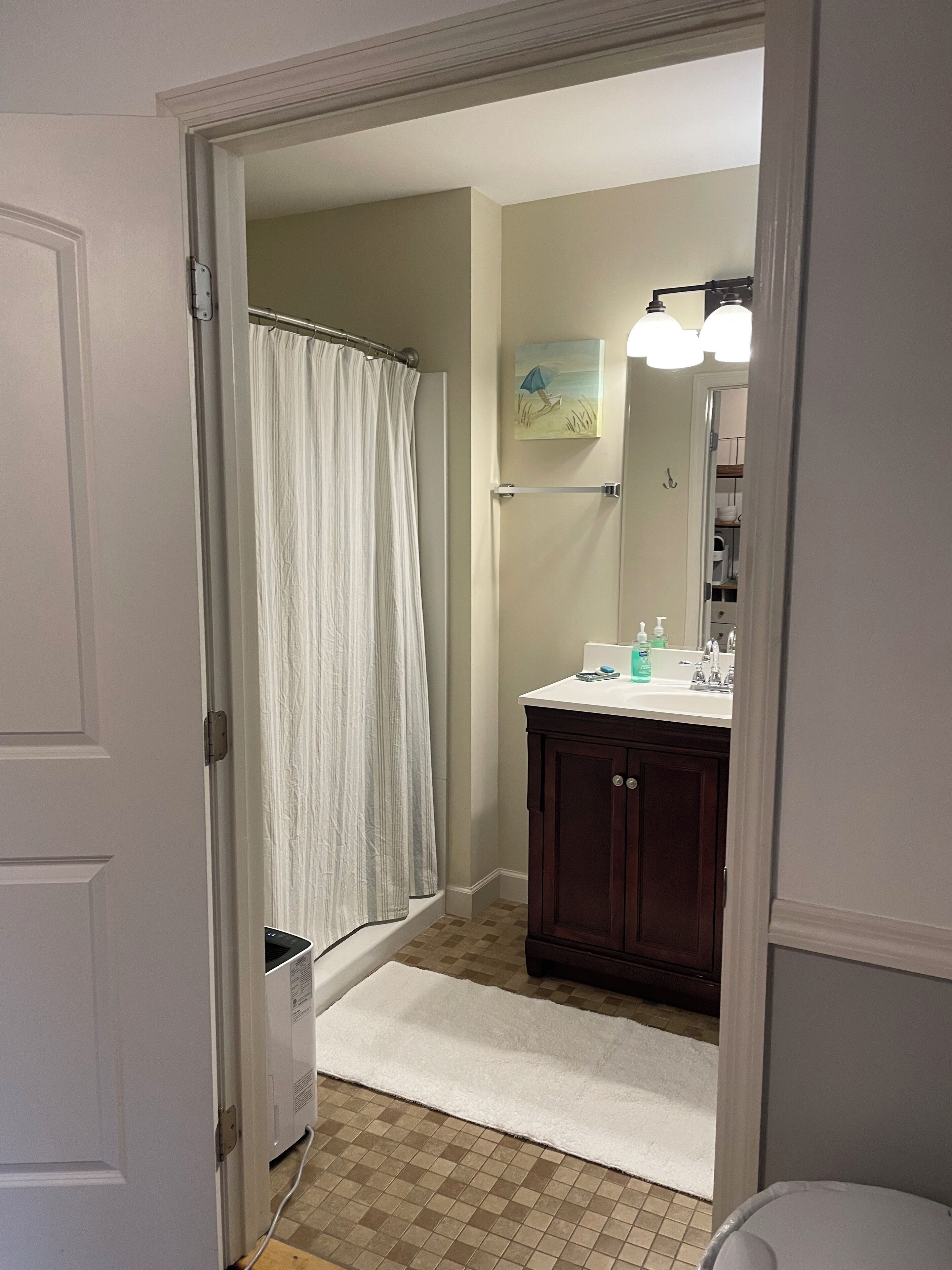 Un bagno con tenda doccia, lavandino con articoli da toilette e specchio con illuminazione.