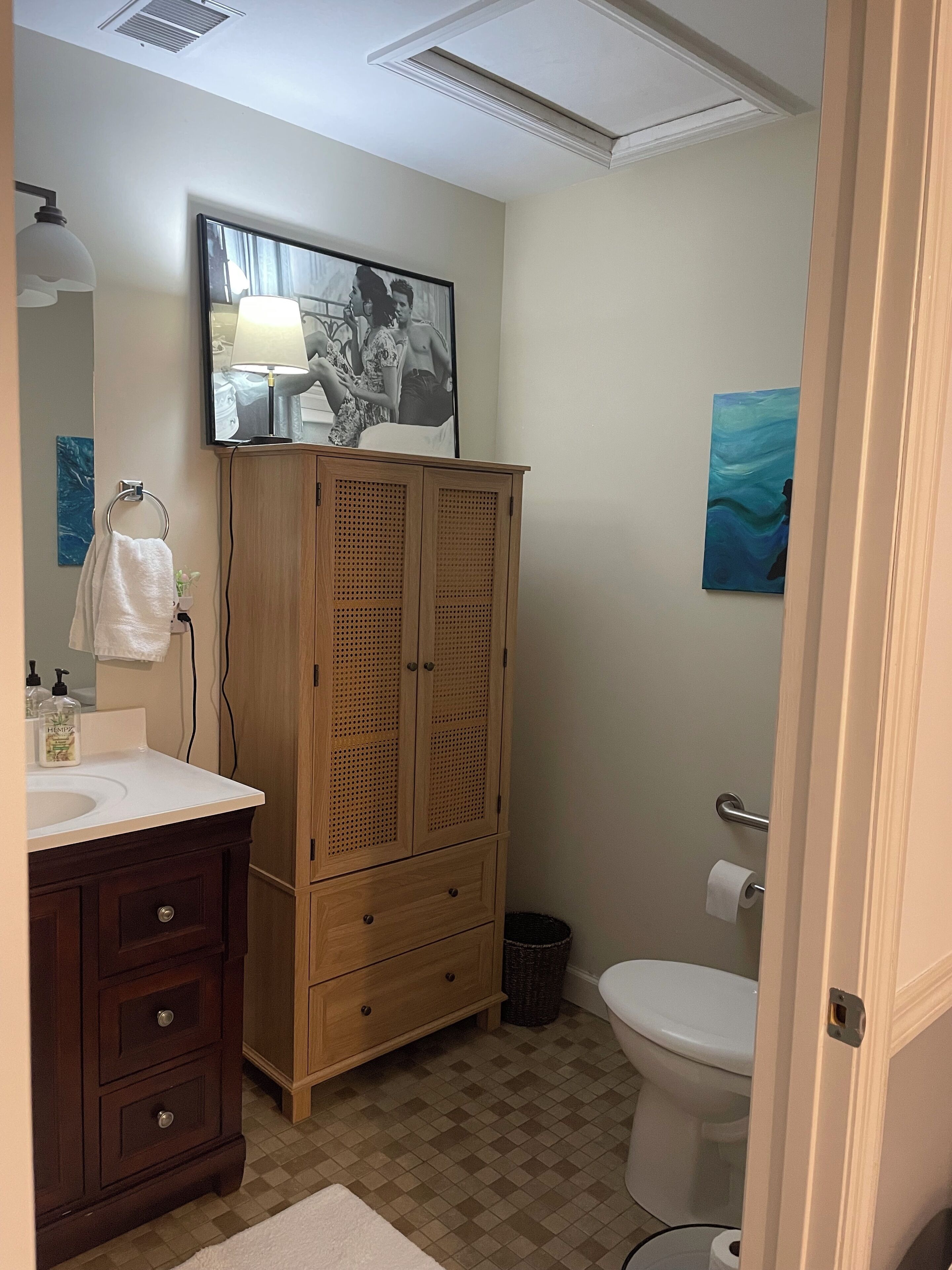 A bathroom with a wooden cabinet, a sink, a toilet, and a mirror.