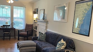 A cozy living room with a dark blue sofa, a small side table, and a fireplace. There are framed pictures on the wall and a large map of Georgia. - Walk to waterfront dining, shops, wine bar. 2 miles from I-95. No pet fee! (Darien)